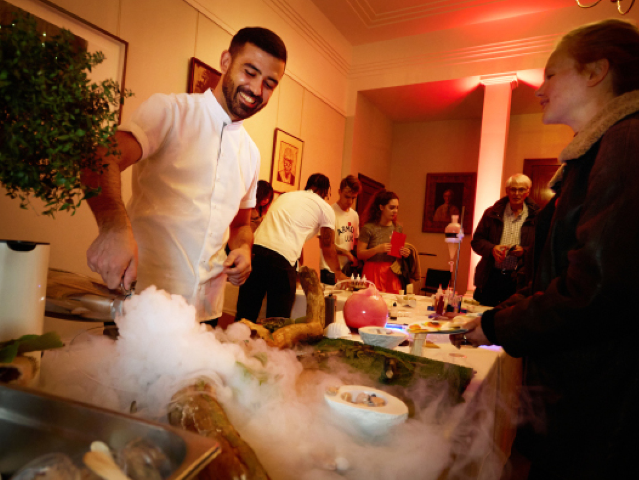 A man in chef's clothing serving food from dry ice in a crowded room