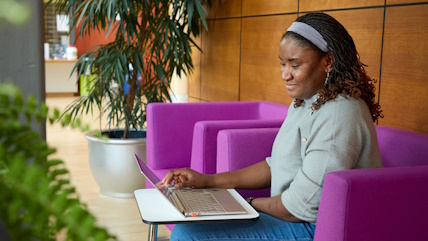 A woman sitting in a bright pink armchair works on a laptop