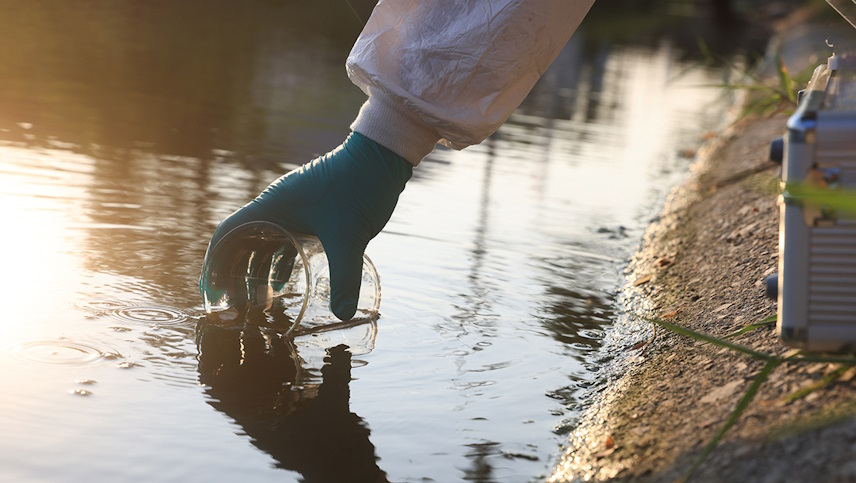 a hand taking a water sample using a jar